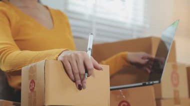 Odasında bir sürü karton kutu olan Asyalı bir kadın. Çevrimiçi ürünler satan genç kadın girişimci, indirme ve çevrimiçi iş aracı 