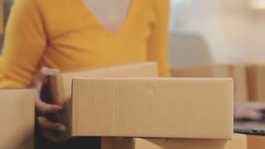 Asyalı bir kadın bir odada sayısız karton kutularla çevrili. Çevrimiçi satış, indirme ve e-ticaret yapan genç bir girişimci olarak rolünü yansıtıyor.