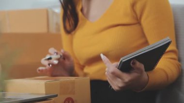 Asyalı bir kadın bir odada sayısız karton kutularla çevrili. Çevrimiçi satış, indirme ve e-ticaret yapan genç bir girişimci olarak rolünü yansıtıyor.