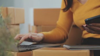 Asyalı bir kadın bir odada sayısız karton kutularla çevrili. Çevrimiçi satış, indirme ve e-ticaret yapan genç bir girişimci olarak rolünü yansıtıyor.