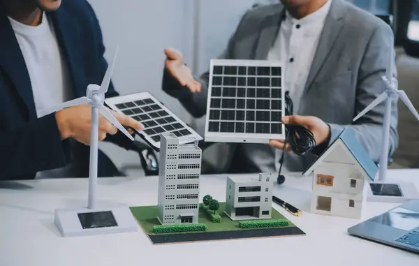 stock image Two Young Engineers Expertise in Solar Cell Installation Meetings and Discussion in The Job. Planning to Install Solar Photovoltaic Panels on Roof Top in The Office Room with Factory Building Plan.