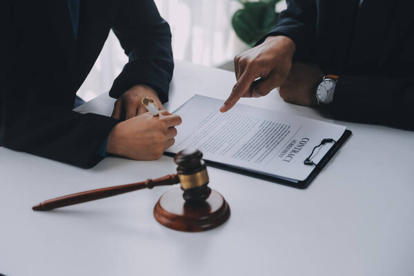 Justice and Law concept. Legal counsel presents to the client a signed contract with gavel and legal law or legal having team meeting at law firm in background