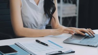 Ofiste oturan Asyalı kadın, hesap makinesi, veriler, çizelgeler ve dokümanlar üzerinde çalışıyor.. 