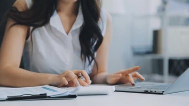 Ofiste oturan Asyalı kadın, hesap makinesi, veriler, çizelgeler ve dokümanlar üzerinde çalışıyor.. 