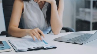 Ofiste oturan Asyalı kadın, hesap makinesi, veriler, çizelgeler ve dokümanlar üzerinde çalışıyor.. 