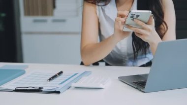 Ofiste oturan Asyalı kadın, hesap makinesi, veriler, çizelgeler ve dokümanlar üzerinde çalışıyor.. 