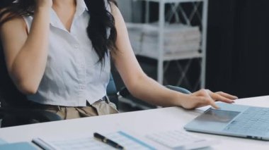 Ofiste oturan Asyalı kadın, hesap makinesi, veriler, çizelgeler ve dokümanlar üzerinde çalışıyor.. 