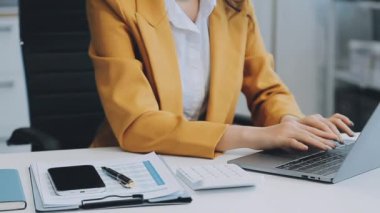 Ofiste oturan Asyalı kadın, hesap makinesi, veriler, çizelgeler ve dokümanlar üzerinde çalışıyor.. 