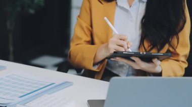 Ofiste oturan Asyalı kadın, hesap makinesi, veriler, çizelgeler ve dokümanlar üzerinde çalışıyor.. 