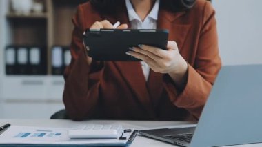 Ofiste oturan Asyalı kadın, hesap makinesi, veriler, çizelgeler ve dokümanlar üzerinde çalışıyor.. 