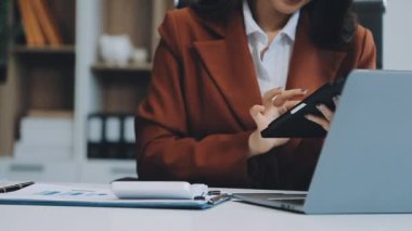 Ofiste oturan Asyalı kadın, hesap makinesi, veriler, çizelgeler ve dokümanlar üzerinde çalışıyor.. 