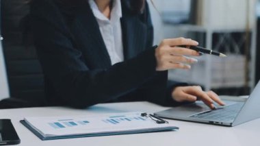 Ofiste oturan Asyalı kadın, hesap makinesi, veriler, çizelgeler ve dokümanlar üzerinde çalışıyor.. 