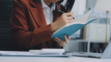 Ofiste oturan Asyalı kadın, hesap makinesi, veriler, çizelgeler ve dokümanlar üzerinde çalışıyor.. 