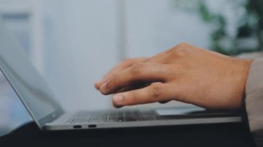 Profesyonel olarak giyinmiş bir işadamı, son teknoloji ve sofistike dekorasyonun üretkenliğini artırdığı modern ve şık bir ofiste aktif olarak dizüstü bilgisayarı üzerinde çalışıyor.