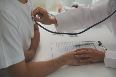 Genç doktor steteskop kullanıyor. Hastanın kalp atışlarını dinle. Kadın bir doktorun erkek bir hastaya muayene yaparken görüntüsü.