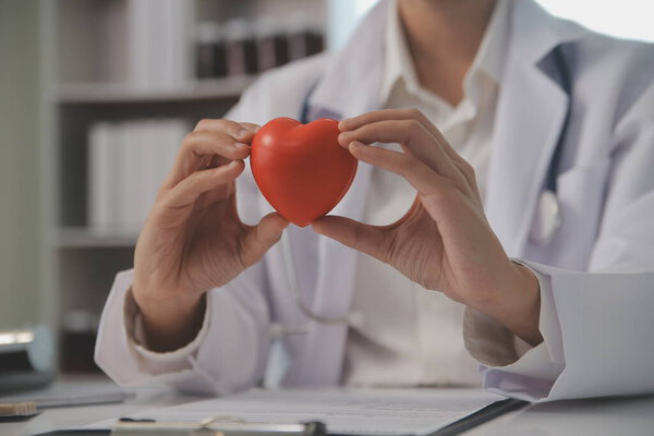 Руки врача женщины с красным сердцем, показывающие символ любви, человеческую поддержку пациенту, поощряющие медицинскую страховку, раннее обследование на предмет здоровья, помощь кардиолога. Закрытие объекта