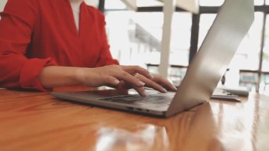 Kırmızı elbiseli Asyalı kadın modern ofisteki dizüstü bilgisayarında çalışıyor.