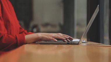 Kırmızı takım elbiseli güzel Asyalı bir kadının portresi modern ofiste dizüstü bilgisayarda çalışıyor.
