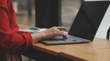 Kırmızı takım elbiseli güzel Asyalı bir kadının portresi modern ofiste dizüstü bilgisayarda çalışıyor.