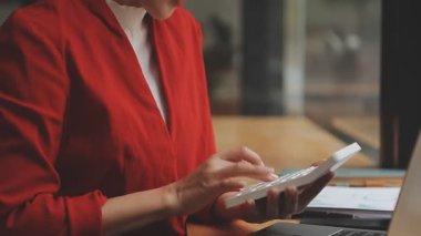 Modern ofiste hesap makinesi kullanan kırmızı elbiseli genç Asyalı kadın.