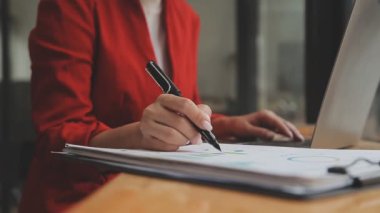 Kırmızı elbiseli Asyalı kadın modern ofisteki dizüstü bilgisayarında çalışıyor.