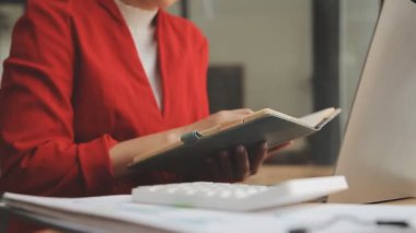 Genç bir iş kadını, iş ve finans kavramlarını ön plana çıkaran bir fon ile çağdaş bir ofiste çalışırken resmedilir..