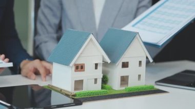 Emlakçı ve müşteriyle ev modeli satın alma, sigorta ya da kredi alma ya da emlak ya da mülkiyet sözleşmesi hakkında tartışıyor.