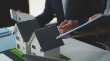 Emlakçı ve müşteriyle ev modeli satın alma, sigorta ya da kredi alma ya da emlak ya da mülkiyet sözleşmesi hakkında tartışıyor.