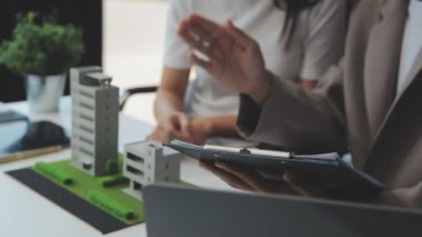 Emlakçı ve müşteriyle ev modeli satın alma, sigorta ya da kredi alma ya da emlak ya da mülkiyet sözleşmesi hakkında tartışıyor.