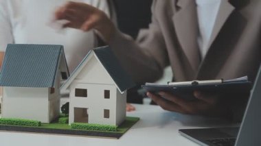 Emlakçı ve müşteriyle ev modeli satın alma, sigorta ya da kredi alma ya da emlak ya da mülkiyet sözleşmesi hakkında tartışıyor.