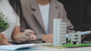 Emlakçı ve müşteriyle ev modeli satın alma, sigorta ya da kredi alma ya da emlak ya da mülkiyet sözleşmesi hakkında tartışıyor.