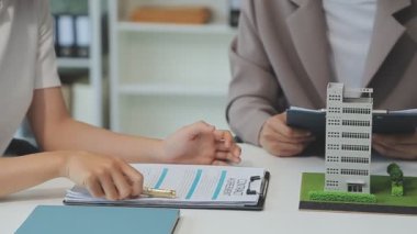 Emlakçı ve müşteriyle ev modeli satın alma, sigorta ya da kredi alma ya da emlak ya da mülkiyet sözleşmesi hakkında tartışıyor.