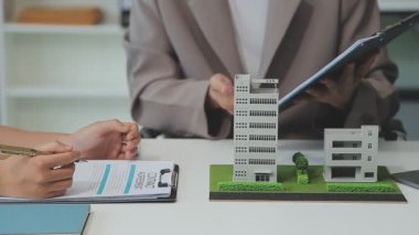 Emlakçı ve müşteriyle ev modeli satın alma, sigorta ya da kredi alma ya da emlak ya da mülkiyet sözleşmesi hakkında tartışıyor.