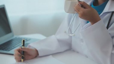 Genç bayan doktor masada oturuyor ve dizüstü bilgisayar kullanıyor..