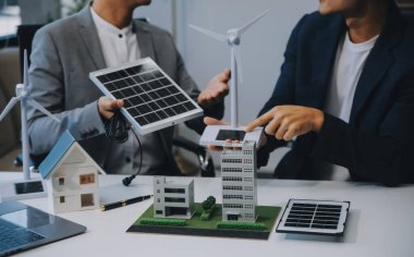 İki Genç Mühendis Güneş Hücresi Kurulum Toplantısı ve İş Tartışması Uzmanı. Ofis Odası 'nda Fabrika İnşaat Planlı Çatı Üzerine Güneş Fotovoltaik Panelleri Kurmayı Planlıyorum.