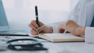 Kadın doktor masada deftere yazı yazıyor.