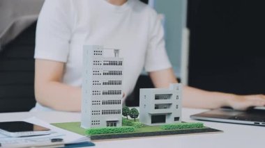 Mimarlar modern bir ofiste bir yapı modeli üzerinde işbirliği yaparken, tasarımcılar inşaat, geliştirme, kentsel planlama, proje yönetimi ve yaratıcı fikirlerle ilgili mimari kavramlar geliştirmeye odaklanıyor.