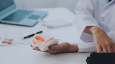 Çağdaş bir klinikte çalışan dişçi, hastaya dişsel prosedürleri gösteren detaylı bir diş modeli gösteriyor.