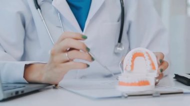 Çağdaş bir klinikte çalışan dişçi, hastaya dişsel prosedürleri gösteren detaylı bir diş modeli gösteriyor.