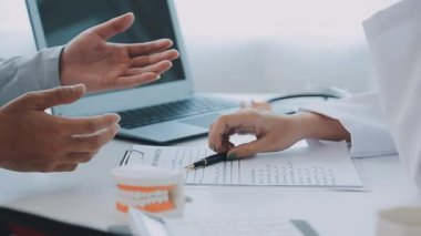 Çağdaş bir klinikte çalışan dişçi, hastaya dişsel prosedürleri gösteren detaylı bir diş modeli gösteriyor.