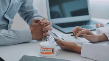 Çağdaş bir klinikte çalışan dişçi, hastaya dişsel prosedürleri gösteren detaylı bir diş modeli gösteriyor.