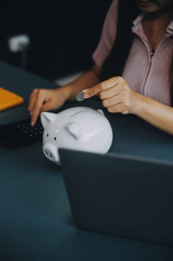 Genç Asyalı kadın emeklilik için para biriktiriyordu. Kumbaradan para biriktiriyordu ve defter, tasarruf konsepti gibi notlar alıyordu..