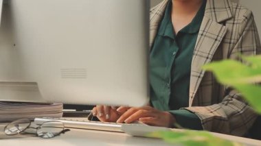 Genç Asyalı iş kadını modern ofis ortamında masa bilgisayarında çalışıyor.