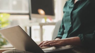 Genç Asyalı iş kadını, modern ofis ortamında dizüstü bilgisayarına odaklanıyor