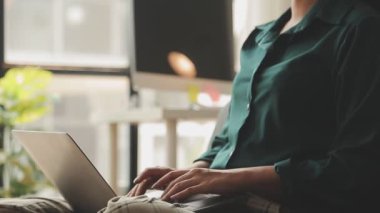 Genç Asyalı iş kadını, modern ofis ortamında dizüstü bilgisayarına odaklanıyor