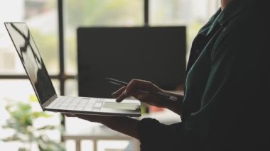 Genç Asyalı iş kadını, modern ofis ortamında dizüstü bilgisayarına odaklanıyor