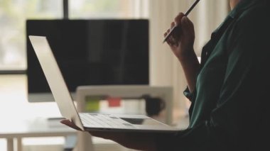 Genç Asyalı iş kadını, modern ofis ortamında dizüstü bilgisayarına odaklanıyor