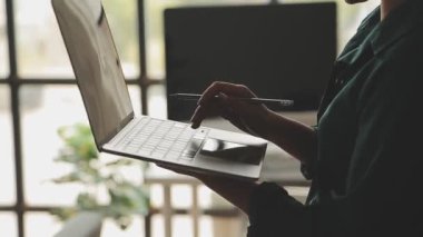 Genç Asyalı iş kadını, modern ofis ortamında dizüstü bilgisayarına odaklanıyor