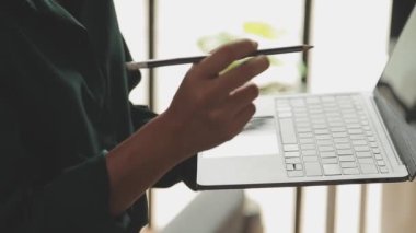 Genç Asyalı iş kadını, modern ofis ortamında dizüstü bilgisayarına odaklanıyor