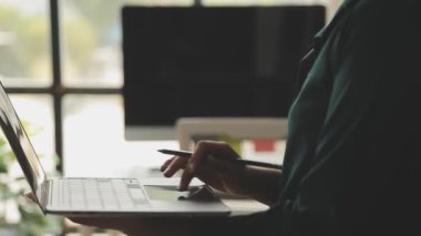 Genç Asyalı iş kadını, modern ofis ortamında dizüstü bilgisayarına odaklanıyor